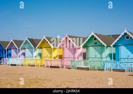 Strandhütten Großbritannien, Blick an einem Sommertag auf eine Reihe farbenfroher traditioneller Strandhütten am Strand in West Mersea, Essex, England, Großbritannien Stockfoto