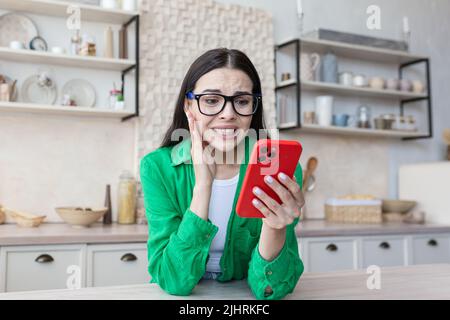 Schockiert junge schöne Frau in Brille Lesung Nachricht vom Telefon, Teenager in der Küche Stockfoto