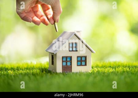 Nahaufnahme Der Hand Putting Coin In House Piggy Bank Stockfoto