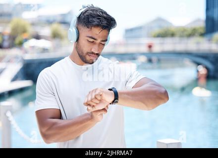 Der junge Sportler verbindet seine smarte Uhr mit seinen Kopfhörern, um beim Laufen oder Joggen Musik zu hören. Gemischter männlicher Athlet, der sein Ziel verfolgt Stockfoto