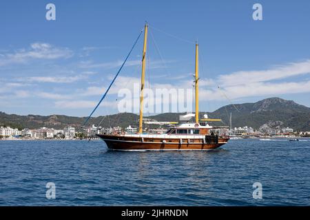 Yacht mit gesenkten Segeln in der blauen Bucht des Mittelmeers auf Marmaris Ferienort und Berge Hintergrund im Sommer Stockfoto