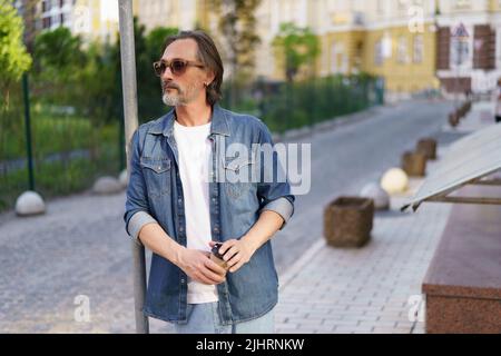 Emotional erschöpft mittleren Alters Krise reifer Mann lehnte sich auf Straßenschild halten Papierbecher Kaffee. Erleben Kater mittleren Alters alkoholischen Mann trinken mit Papierbecher, um Alkohol zu verstecken. Stockfoto