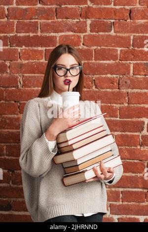 Schönes Mädchen trinkt Kaffee-to-go auf Bücher Stockfoto