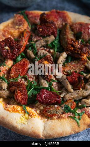 Nahaufnahme einer leckeren Tofu-Pizza mit getrockneten Tomaten und Rucola. Veganes Essen Stockfoto