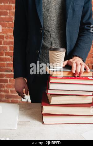 Nicht erkennbarer Mann, der bei Büchern und Kaffee steht Stockfoto