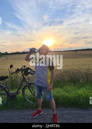 Schöner junger Profi-Radfahrer in Radbekleidung und Schutzhelm gekleidet Gefühl frei und glücklich, Trinkwasser aus der Flasche, genießen Stockfoto