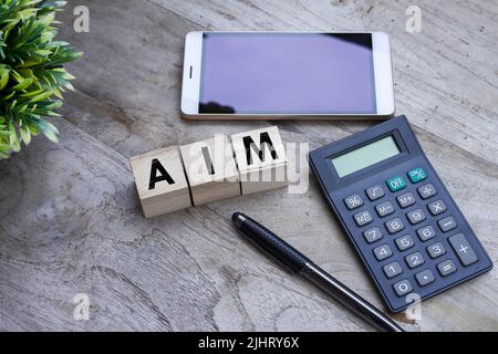Das Wort "zielen" auf kleine Holzwürfel mit einem Rechner, ein Smartphone auf einem Holztisch Stockfoto