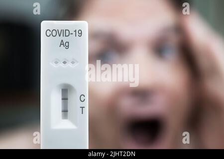 Covid-19-positiver Schnelltest mit verschwommenem männlichem Gesicht, schreiend. Stockfoto