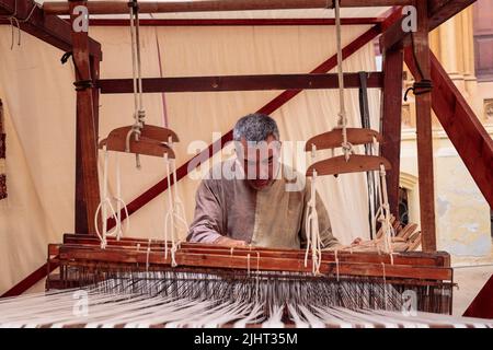 Mittelalterliche Technik. Mann, der die Tuchweberei mit einem traditionellen handbetriebenen Holzwebstuhl aus Naturfasern demonstriert. Mdina Medieval Festival, Malta Stockfoto