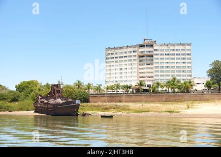 Dec 30, 2021, Colon, Entre Rios, Argentinien: Blick von einem Boot auf dem Uruguay-Fluss, Intersur-Hotel und einem verlassenen rostigen Boot. Stockfoto