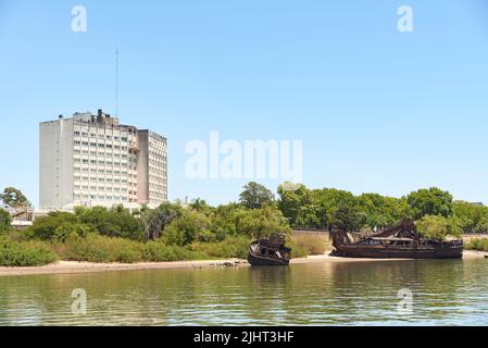 Dec 30, 2021, Colon, Entre Rios, Argentinien: Blick von einem Boot auf dem Uruguay-Fluss, Intersur-Hotel und verlassene rostige Schiffe. Stockfoto