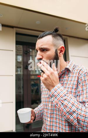 Junge Hipster rauchen mit einer Tasse Kaffee im Freien Stockfoto