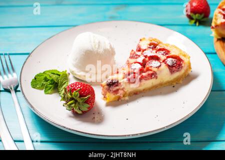 Hausgemachte Erdbeerpudding-Tarte mit Erdbeere und Eis auf blauem Holzhintergrund. Stockfoto
