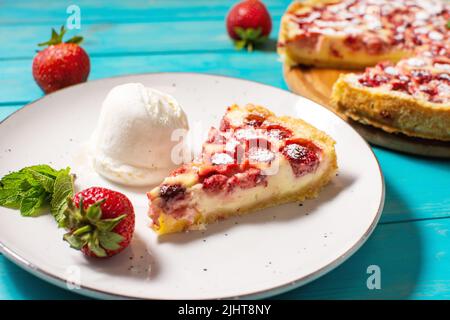 Hausgemachte Erdbeerpudding-Tarte mit Erdbeere und Eis auf blauem Holzhintergrund. Stockfoto