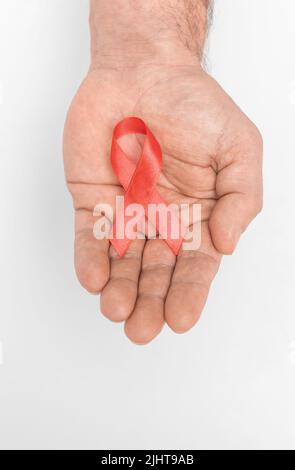 Rotes Band Bogen Bewusstsein auf mans Hand isoliert auf weißem Hintergrund. HIV, AIDS Welttag. Soziales Leben Themen Konzept. Konzept des AIDS-Fonds. Gesundheits- und Medizinkonzept. Stockfoto