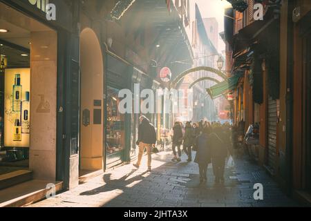 Eine geschäftige Straße mit morgendlicher Sonneneinstrahlung, die auf eine Menschenmenge in Bologna, Italien, herabscheint Stockfoto