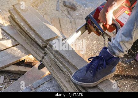 Schneiden alter Holzspanplatten mit elektrischer Kettensäge, Splitter fliegen in der Luft, Nahaufnahme Detail Stockfoto