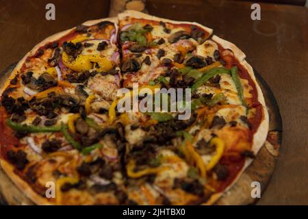 Pilzpizza mit Fleisch und Paprika frisch gebacken auf einem Holzbrett und Holztisch für den Kunden serviert. Tisch in einem Holzofen, serviert in einem r Stockfoto