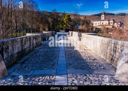 Die Puente del Perdón - Brücke der Begnadigung, ist eine steinerne Brücke über den Fluss Lozoya. Im Hintergrund das Monasterio de Santa María de El Paular - Stockfoto