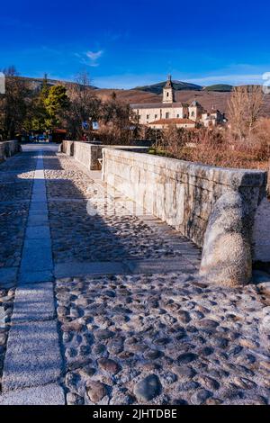 Die Puente del Perdón - Brücke der Begnadigung, ist eine steinerne Brücke über den Fluss Lozoya. Im Hintergrund das Monasterio de Santa María de El Paular - Stockfoto