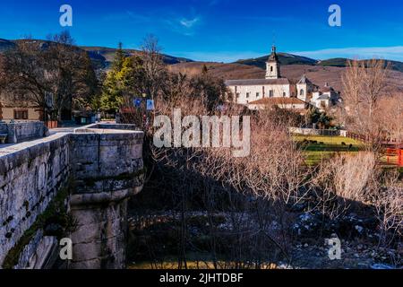 Die Puente del Perdón - Brücke der Begnadigung, ist eine steinerne Brücke über den Fluss Lozoya. Im Hintergrund das Monasterio de Santa María de El Paular - Stockfoto