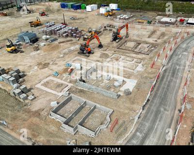 Pontypridd, Wales - Juli 2022: Luftaufnahme von mechanischen Baggern, die neben den Basen für neue Häuser auf einer Wohnsiedlung in Südwales geparkt sind. Stockfoto