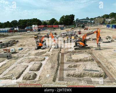 Pontypridd, Wales - Juli 2022: Luftaufnahme von mechanischen Baggern, die neben den Basen für neue Häuser auf einer Wohnsiedlung in Südwales geparkt sind. Stockfoto