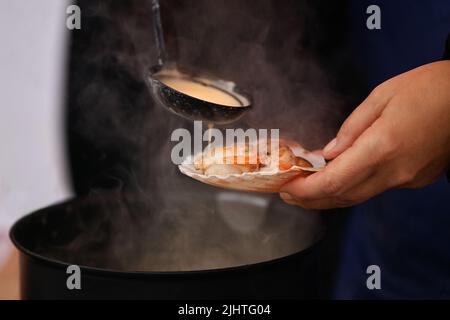 Der Verkäufer gießt weiße Sauce auf die Jakobsmuscheln Stockfoto