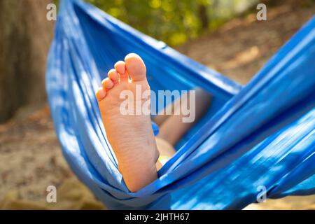 Kinderfuß in einer Hängematte, rollend im Wald im Sommer in der Sonne, Rest in einer Hängematte, ein Fuß in einer Hängematte, Rest im Wald Stockfoto