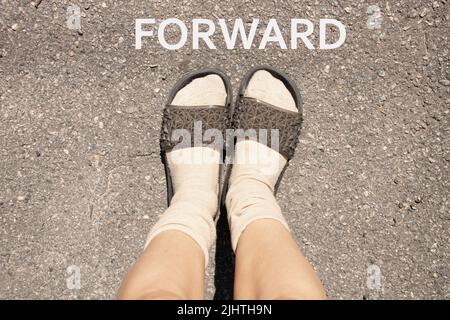 Weibliche Füße in Socken und Pantoffeln auf grauem Asphalt, weibliche Füße auf der Straße Stockfoto