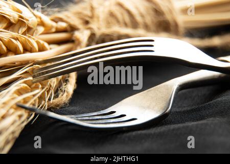 Alte Gabeln und Dornen aus trockenem Weizen auf schwarzem Hintergrund, Nahaufnahme, Küchenutensilien, Vintage-Besteck, Tischdekoration Stockfoto