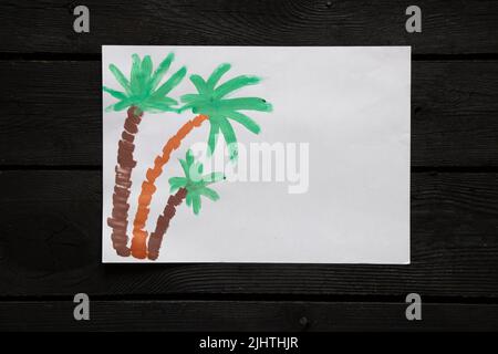 Drei Palmen, die mit Farbe auf weißem Papier gemalt sind, liegen auf einem schwarzen Holztisch, Palmen, die mit Farben bemalt sind, Kinderzeichnungen, Palmen, Meeresruhe Stockfoto