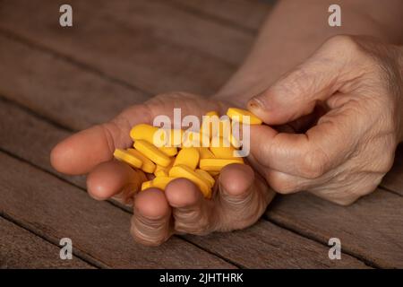 Großmutter hält gelbe Pillen in den Händen auf einem Holztisch, Pillen in den Händen und Frauen liegen und Medizin Stockfoto