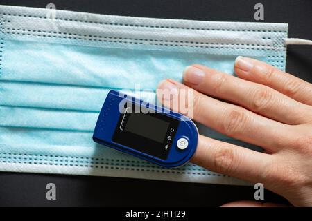 Frau Finger Pulsoximeter und Einweg-medizinische Maske auf isoliertem Hintergrund, Messen Blut Sauerstoffgehalt, Oxometer, Gesundheit Stockfoto