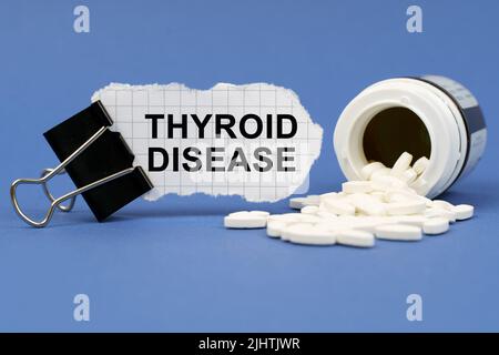 Medizinkonzept. Auf der blauen Oberfläche liegt ein Glas Pillen und eine Klemme mit Papier, auf dem geschrieben ist - Schilddrüsenerkrankung Stockfoto