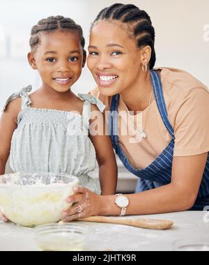 Mummys kleine Helferin in der Küche. Eine attraktive junge Mutter, die sich mit ihrer Tochter verklebt und ihr zu Hause beim Backen in der Küche hilft. Stockfoto