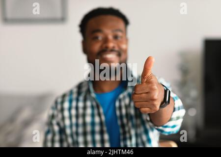 Fröhlicher Afrikanischer Amerikanischer Kerl Gestikuling Thumbs Up Sitting At Home Stockfoto