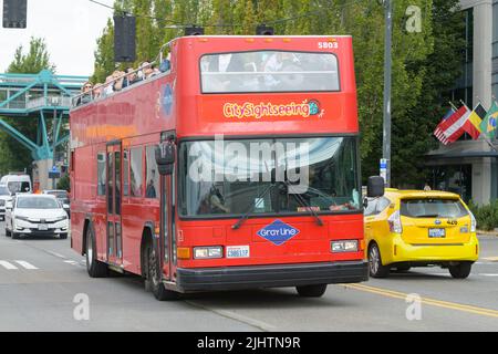 Seattle - 17. Juli 2022; Ein roter City Sightseeing Doppeldeckerbus der Gray Line fährt mit fröhlichen Touristen über die Hafenpromenade von Seattle Stockfoto