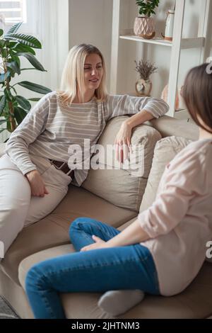 Junge Freundinnen reden, lächeln zusammen, sitzen auf Sofa A Stockfoto
