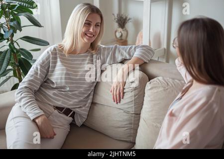Junge Freundinnen reden, lächeln zusammen, sitzen auf Sofa A Stockfoto