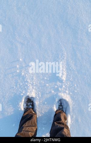 Niedriger Abschnitt einer Person, die an einem sonnigen Tag im Winter im Schnee steht, von oben betrachtet. Speicherplatz kopieren. Stockfoto