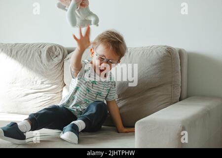 Ein Kind mit Autismus in einer Brille sitzt auf dem Sofa und traurig, wütend Stockfoto