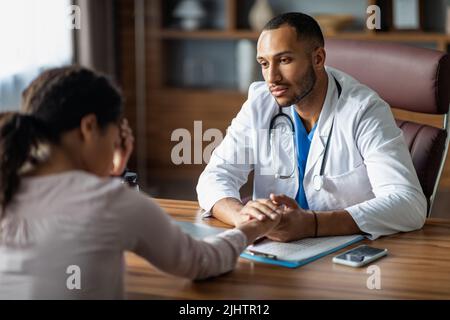 Arzt, der mit einer verärgerten schwarzen Patientin sprach und die Hand hielt Stockfoto