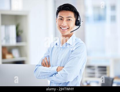 Porträt eines asiatischen Callcenter-Agenten, der ein Headset trägt, während er im Büro arbeitet, während er mit gekreuzten Armen steht. Selbstbewusster und lächelnder Geschäftsmann Stockfoto