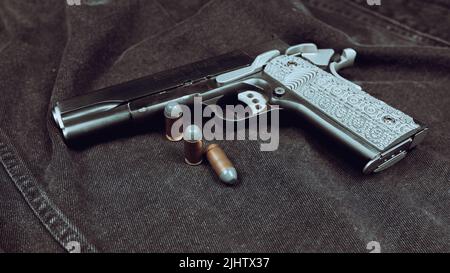 Pistole des Modells 1911 und drei Patronen (.45 ACP) auf schwarzem Denim-Hintergrund Stockfoto