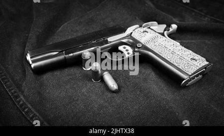 Modell 1911 Pistole und drei Patronen (.45 ACP) auf schwarzem Denim-Hintergrund, monochromes Foto Stockfoto