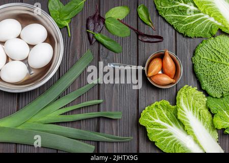 Eier in Metallschüssel, Lauch und Schalotten, Spinatblätter und wirsing-Kohl. Flach liegend. Holzhintergrund. Stockfoto