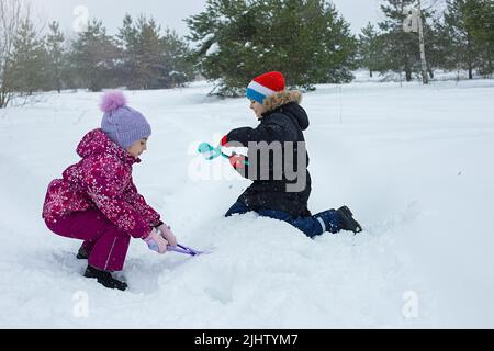 Ein Junge und ein Mädchen sind im Winter Park im Freien und machen Schneebälle mit Plastikmodellierwerkzeugen. Stockfoto