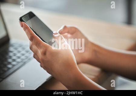 Eine Frau, die ihr Smartphone benutzt, während sie in einem Café arbeitet. Stockfoto