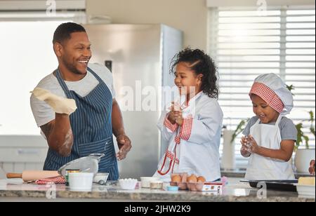 Der Erfolg beim Backen bringt Kindern Vertrauen in ihre kreativen Fähigkeiten bei. Ein Vater, der mit seinen beiden Töchtern zu Hause bäckt. Stockfoto